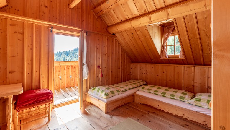 Schlafzimmer, © Wiener Alpen / Christian Kremsl Schlafzimmer mit Holzvertäfelung, zwei Betten, einem Fenster und offener Tür zum Balkon.