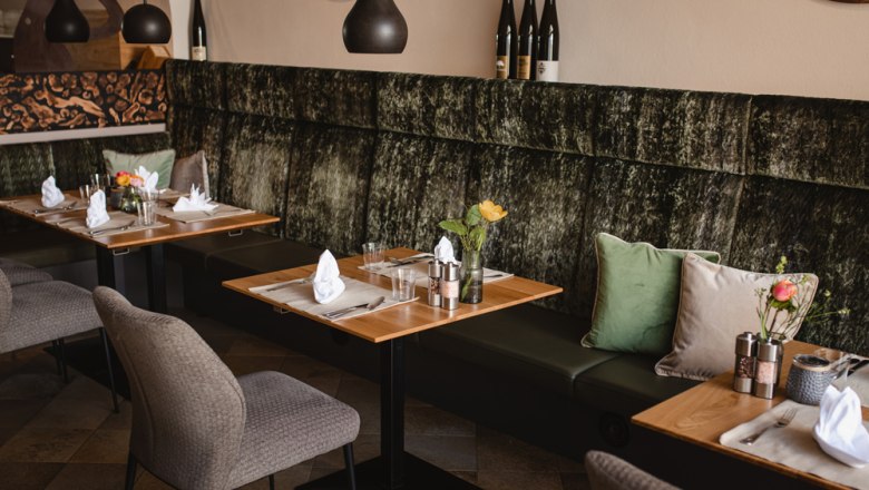 Moderne Gastzimmer und Vinothek, © Niederösterreich Werbung/Daniela Führer Ein modernes Restaurant mit stilvoll gedeckten Tischen, Polsterbänken und Weinflaschen als Dekoration.