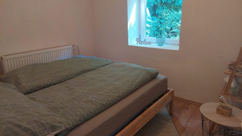 Schlafzimmer, © Wein-Bleibe Ein gemütliches Schlafzimmer mit einem Bett, einem Fenster mit Blick ins Grüne und einem Bild an der Wand.