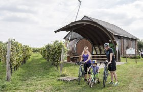 Erlebnisweingartl Hohenruppersdprf, © Weinviertel Tourismus GmbH / Herbst Eine Familie mit Fahrrädern vor einem Weingut mit großem Fass in Hohenruppersdorf.