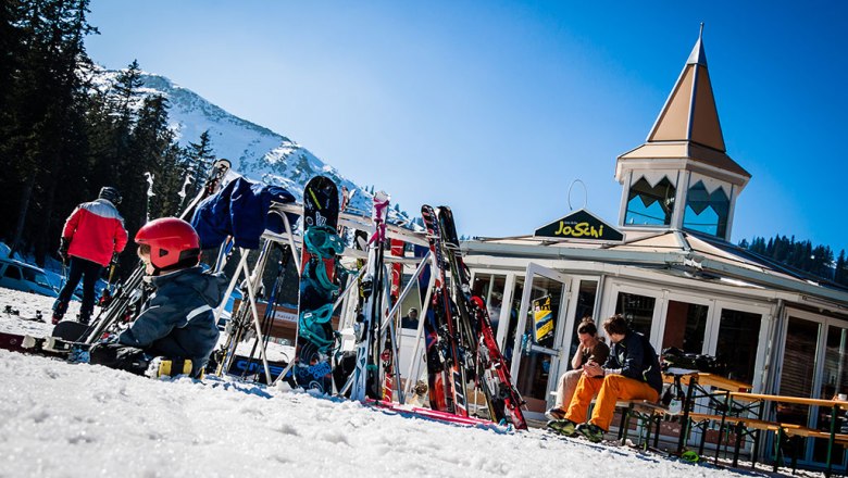 JoSchi-Bar, © JoSchi-Bar Skifahrer vor der JoSchi-Bar mit Skiern und Snowboards im Schnee.