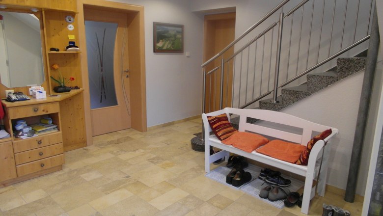 Eingangsbereich Lugerhof, © Lugerhof Eingangsbereich mit Holzkommode, Bank mit Kissen und Treppe.