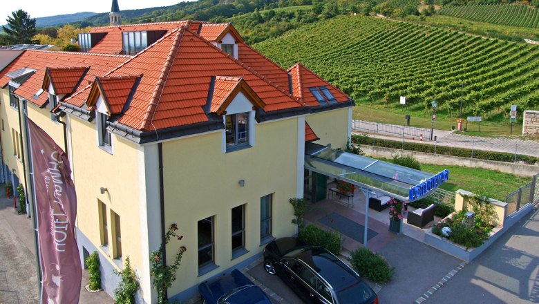 Aussenansicht Hotel Turmhof, © Hotel Turmhof Außenansicht des Hotel Turmhof mit roten Dächern und umliegenden Weinbergen.