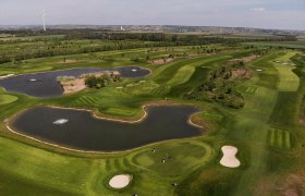 GolfRange in Bockfließ, © GEPA Pictures Luftaufnahme eines Golfplatzes mit Teichen und Windrad im Hintergrund.