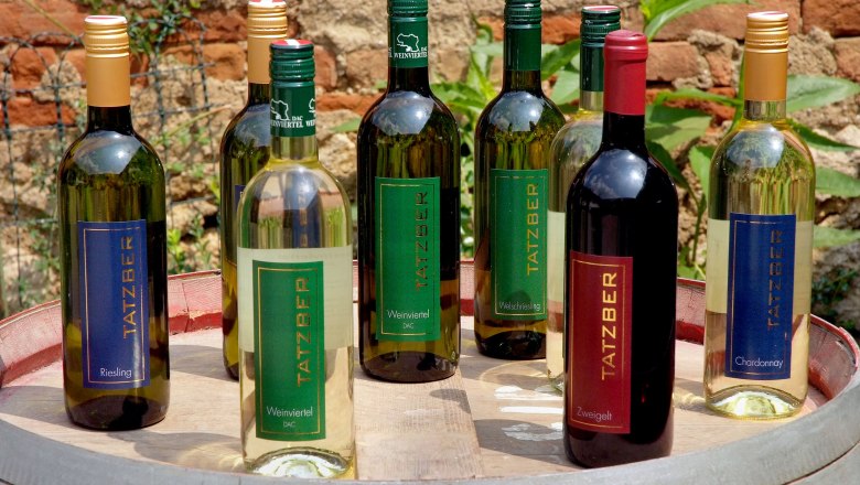 Weinsortiment, © Seymannfilm Verschiedene Tatzber Weinflaschen auf einem Fass im Freien.