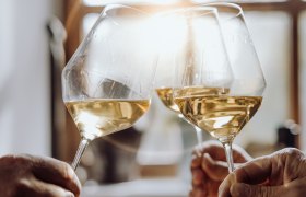 Weinglas anstoßen, © Weinviertel Tourismus GmbH / Creating Click Drei Personen stoßen mit Weißweingläsern an, Sonnenlicht im Hintergrund.