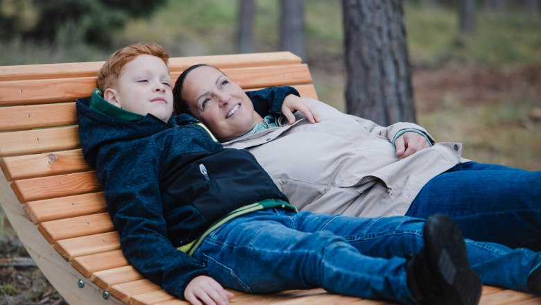 Entspannung pur im Heilwald Göttweig, © Alexander Pfeffel Photography Zwei Personen liegen entspannt auf einer Holzbank im Wald.