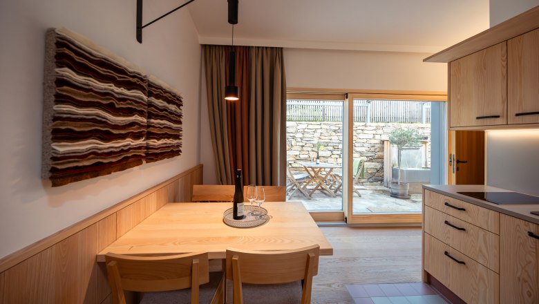 Weinviertler Kellerstöckl Weingut Hindler, © Niederösterreich Werbung / Maximilian Pawlikowsky Innenansicht eines modernen Essbereichs mit Holzmöbeln und Wandkunst, Blick auf eine Terrasse durch eine Glastür.