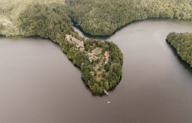 Abkühlung, Stausee Dobra, Ruine Dobra, Waldviertel, © Foto by Patrick Wasshuber | CC-BY 4.0 Drohnenaufnahme der bewaldeten Halbinsel mit der Ruine Dobra im Stausee Dobra; die Ruine liegt von Wasser umgeben, mit kleinen Booten und Wiesenflächen am Ufer.