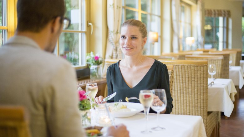 Alpen-Aktiv-Landgasthof zur Schubertlinde, © Patrick Haberler Ein Paar beim Abendessen in einem gemütlichen Restaurant mit großen Fenstern und Kerzenlicht.