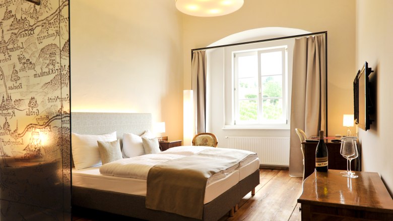 Zimmer, © Freigut Thallern Elegantes Hotelzimmer mit Doppelbett, Holzboden und großem Fenster.