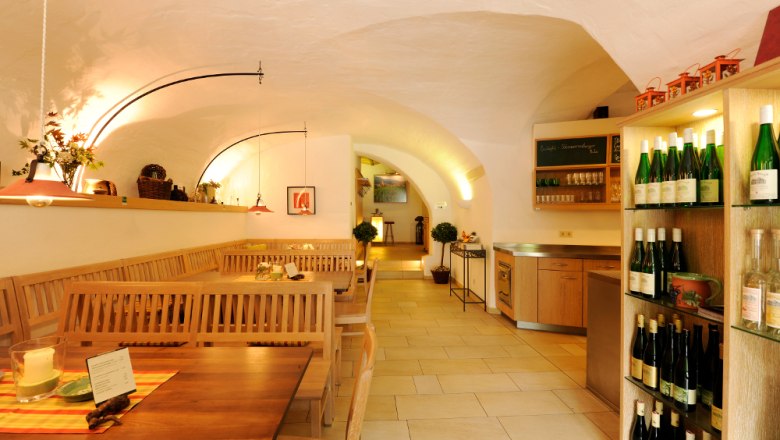 Heurigenlokal, © Steve Haider Innenansicht eines gemütlichen Heurigenlokals mit Holztischen und Weinregalen.