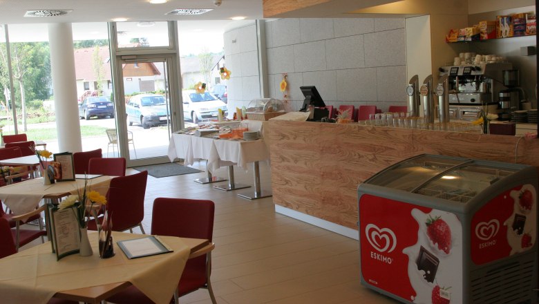 Cafeteria im Neuro Rehab Allentsteig, © Stadtgemeinde Allentsteig Innenansicht eines Cafés mit roten Stühlen, Holztresen und Eiskühltruhe.