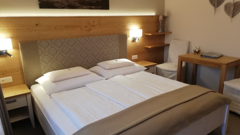 Familienzimmer, © Familie Rosinger Gemütliches Hotelzimmer mit Doppelbett, Holzmöbeln und Wanddekoration.