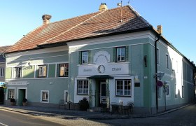 Zum weißen Rössl, © Roman Zöchlinger Ein traditionelles Gasthaus mit grüner Fassade und dem Namen 'Zum weißen Rössl'. Vor dem Gebäude stehen Tische und Stühle.
