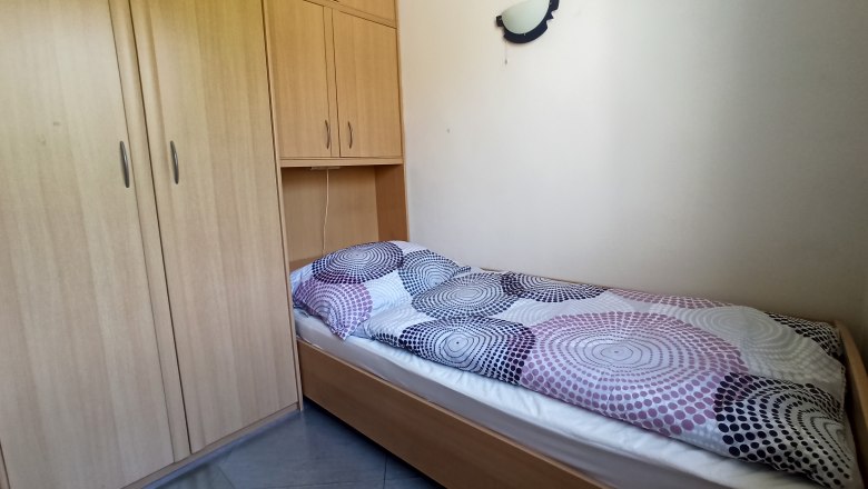 Schlafzimmer, © Multimedia Lauda Ein einfaches Schlafzimmer mit einem Einzelbett und einem großen Holzschrank.