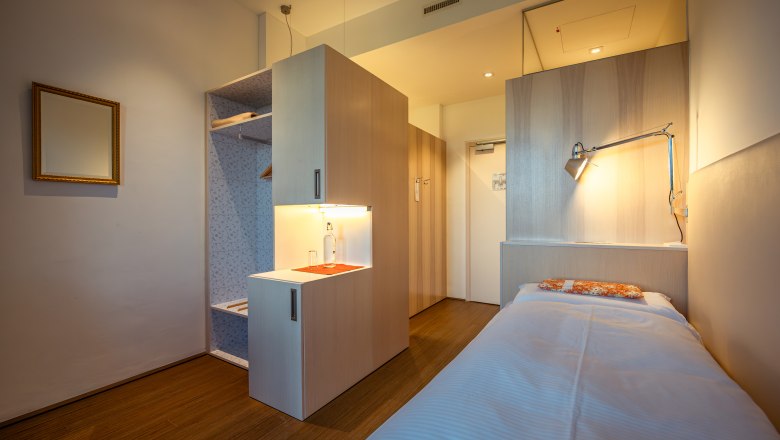 Refugium Hochstrass, © Niederösterreich Werbung / Maximilian Pawlikowsky Modernes, minimalistisches Hotelzimmer mit Einzelbett, Holzfußboden und Schreibtischlampe.