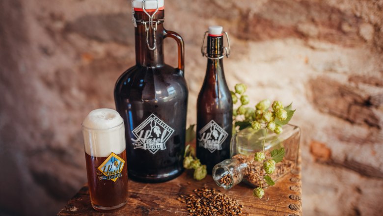 Haselbräu, © Niederösterreich Werbung/Daniela Führer Bierflaschen und Glas mit Haselbräu-Logo, Hopfen und Malz auf Holztisch.