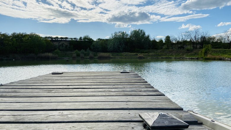 Idyllisches Fischerparadies, © Weinstraße Weinviertel Holzsteg am Ziegelofenteich in Zellerndorf, umgeben von Bäumen und blauem Himmel mit Wolken.