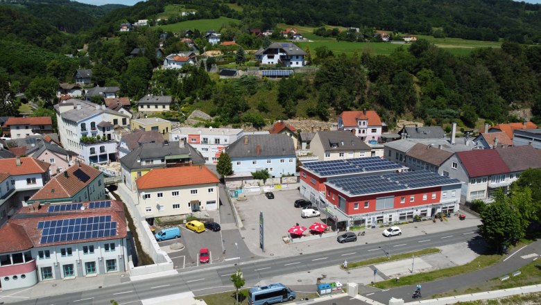Cafe und Bäckerei Lechner Luftaufnahme, © Bäckerei Leichner Luftaufnahme eines Dorfes mit Gebäuden, Straßen und grüner Landschaft im Hintergrund.