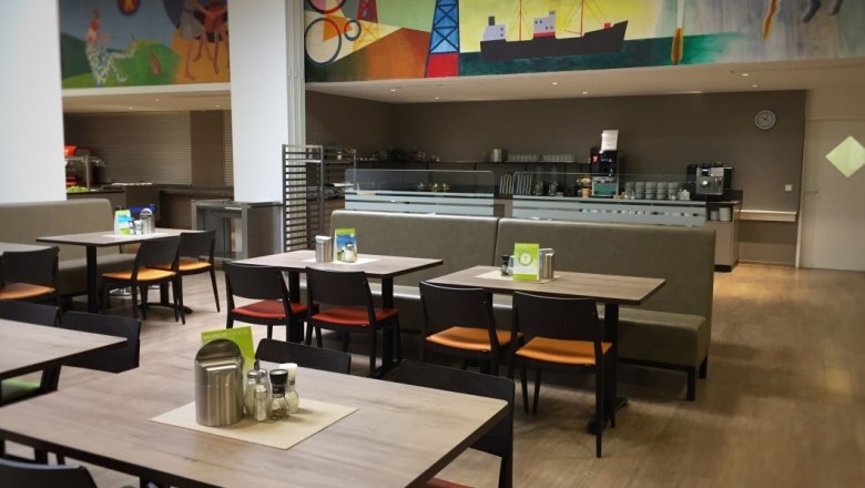 Restaurant, © Stadthotel Hollabrunn Innenansicht eines Restaurants mit leeren Tischen und Stühlen, bunte Wandmalerei im Hintergrund.