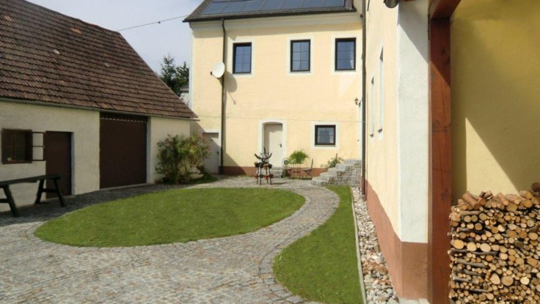Innenhof, © Haus Sonnenuhr, Lackenbauer Ein gepflegter Innenhof mit gepflastertem Weg, Rasenfläche und gelben Gebäuden.