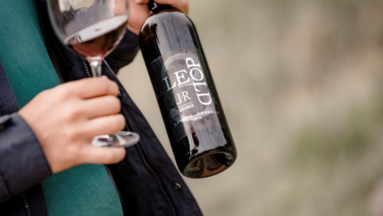 Winzerhof Leo Rögner, © Astrid Bartl Person hält eine Weinflasche und ein Glas Rotwein.