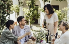 Genießerhof Haimer, © Weinviertel Tourismus GmbH / Sophie Menegaldo Vier Personen sitzen an einem Tisch im Freien und genießen Wein und Brot.
