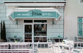 Außenansicht, © Heim.Spiel/Kathi Kurzbauer Außenansicht eines Cafés mit Terrasse und Sitzgelegenheiten.