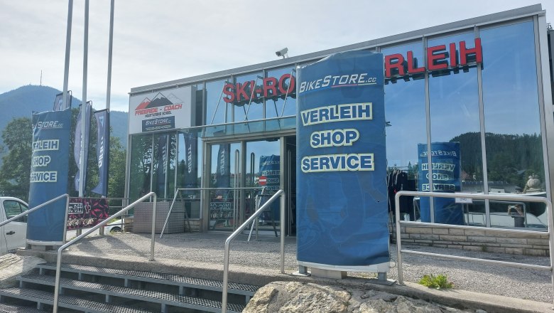 Bikestore.cc, © Bikestore.cc Eingang eines Sportgeschäfts mit Verleih, Shop und Service. Im Hintergrund Berge.
