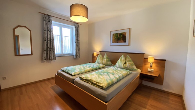 Ferienwohnung Traube, © Trachsler Schlafzimmer mit Doppelbett, Holzboden, Nachttischen und Lampe.
