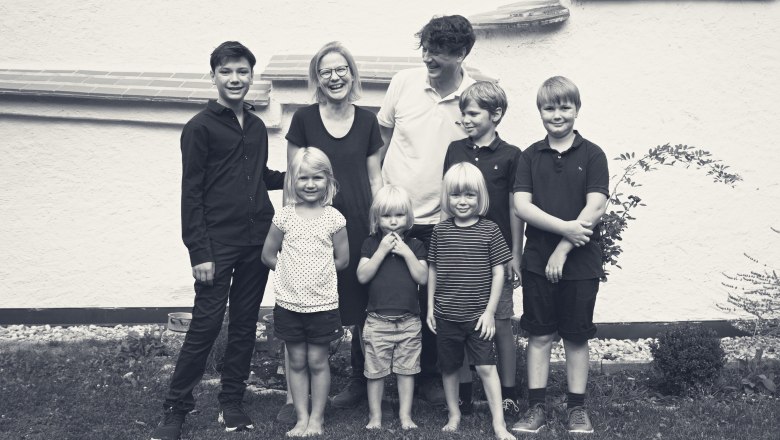 Fam. Pölzer, © Monika Pölzer Eine Familie mit sieben Personen steht lächelnd vor einer weißen Wand im Freien.