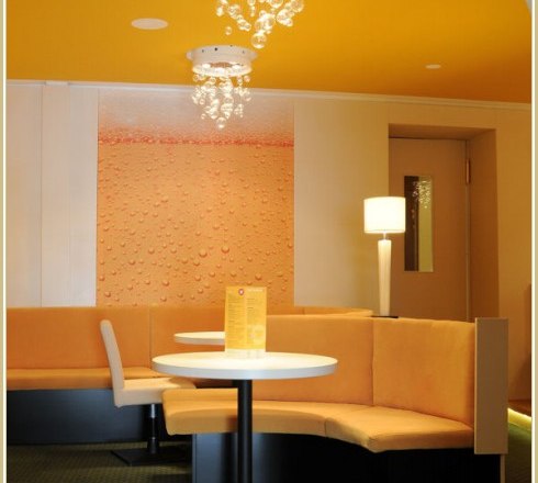 Café-Pub Rathaus Innenansicht, © Café-Pub Rathaus Innenansicht eines modernen Cafés mit gelben Wänden, runden Tischen und gepolsterten Sitzbänken.