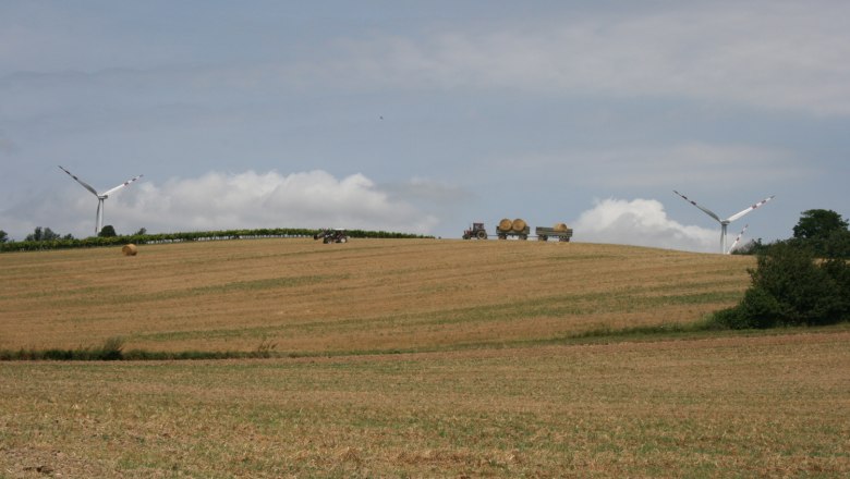 Sanfte Hügel laden zum Wander ein, © Gemeinde Kreuzstetten Landschaft mit Windrädern, Traktor und Heuballen auf einem Feld.