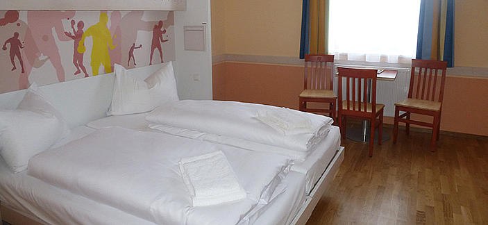 JUFA Hochkar, © JUFA Hochkar Sport Resort Hotelzimmer mit Doppelbett, zwei Stühlen und einem Tisch vor einem Fenster.