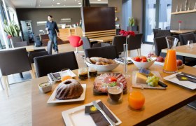 Weingut Sonnenhügel, © Astrid Bartl Frühstückstisch mit Gebäck, Aufschnitt, Käse, Obst und Saft in einem modernen Café.