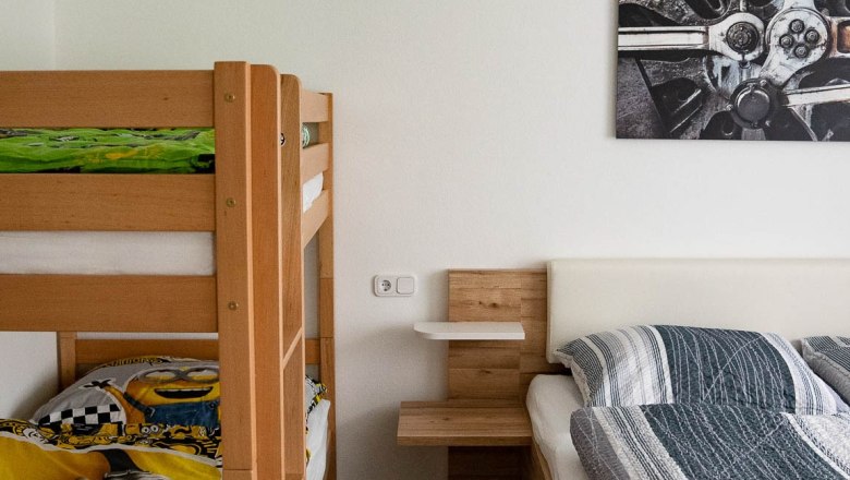 Schlafzimmer (Doppelbett + Stockbett), © Manuel Hahn Ein Schlafzimmer mit einem Etagenbett und einem Doppelbett aus Holz. An der Wand hängt ein Bild mit einem technischen Motiv.