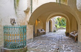 Durchgang, © Renaissancehotel “ Raffelsberger Hof “ Ein steinerner Durchgang mit Bänken, einer Laterne und einem verzierten Brunnen.