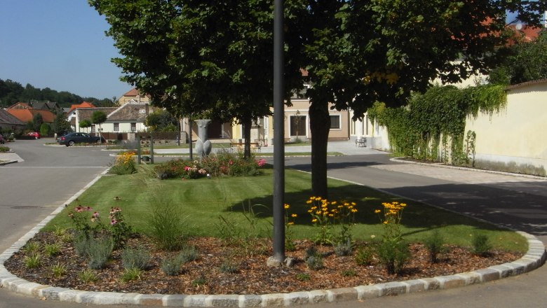 Venus von Eggendorf, © Stadtgemeinde Maissau Ein gepflegtes Blumenbeet mit gelben Blumen und Bäumen in einer ruhigen Wohnstraße.