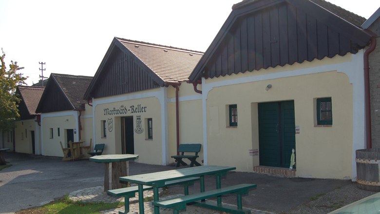 Markwardkeller, © Regina Baumgartner Traditionelle Weinkeller mit Holzbänken und Tischen im Freien.