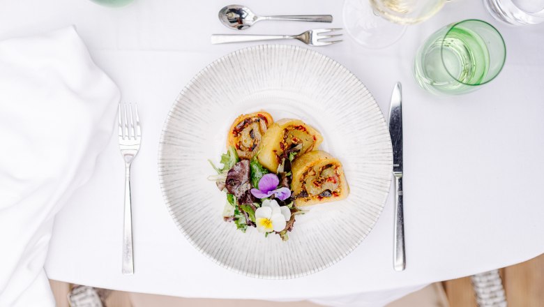 Gefüllte Erdäpfelroulade, © Niederösterreich Werbung/Mara Hohla Ein Teller mit gefüllter Erdäpfelroulade und Salat auf einem gedeckten Tisch.