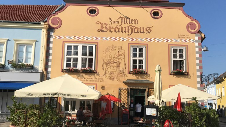 Brauhaus Neunkirchen, © Johann Gansterer Fassade eines traditionellen Brauhauses mit Sonnenschirmen und Sitzbereich im Freien.