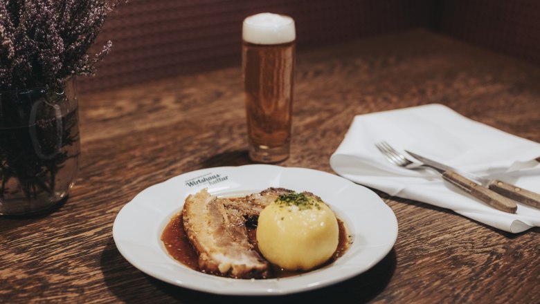 Schweinsbraten mit Waldviertler Knödel, © Niederösterreich Werbung/David Schreiber Ein Teller mit Schweinsbraten und Waldviertler Knödel, daneben ein Glas Bier auf einem Holztisch.