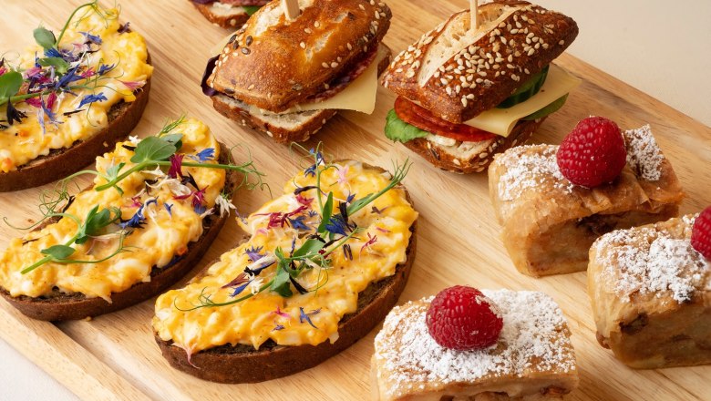 Feine Kaffeepausen bei einem Seminar, © Sporthoel Semmering Verschiedene Snacks auf einem Holzbrett, darunter belegte Brote, Sandwiches und Gebäck mit Himbeeren.