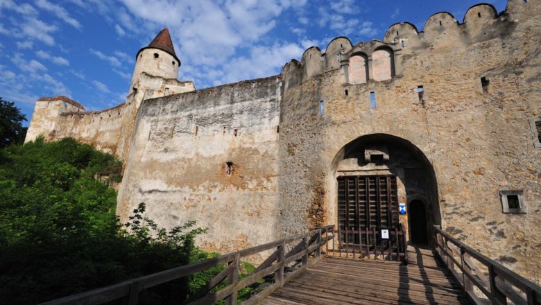 Burg Seebenstein, © POV Eingangstor einer alten Burg mit Holztor und Zinnenmauer, blauer Himmel im Hintergrund.