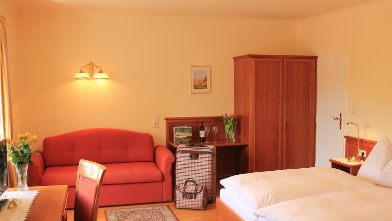 Doppelzimmer Superior, © Schendl Ein gemütliches Hotelzimmer mit Doppelbett, rotem Sofa, Holzmöbeln und Blumen.
