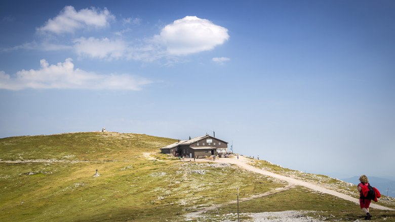 Fischerhuette Schneeberg, © WA/Franz Zwickl Eine Berghütte auf einem Hügel mit blauem Himmel und Wolken im Hintergrund.