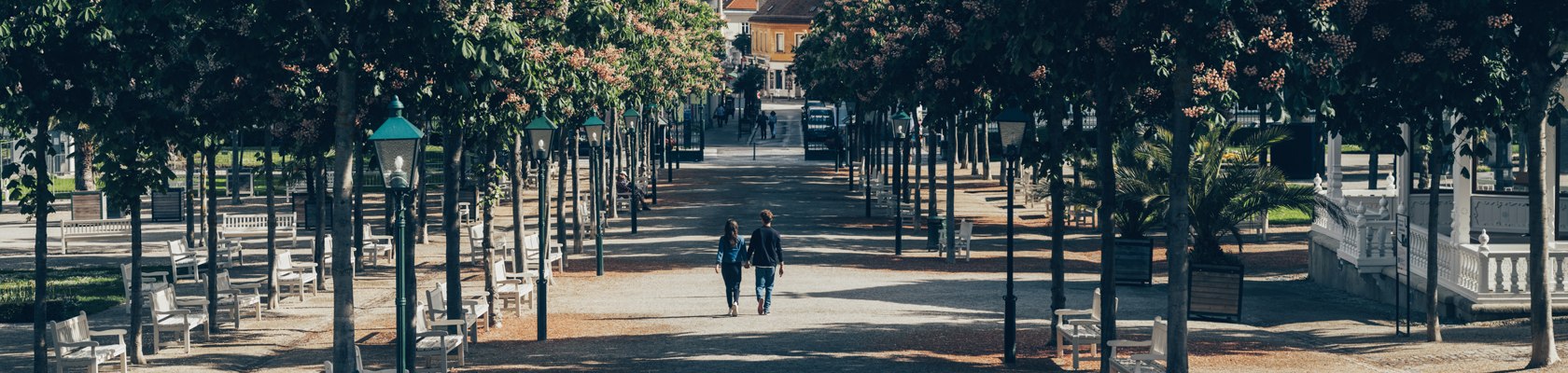 Selected Stays, © Ian Ehm Ein Pärchen geht im Kurpark Baden spazieren. Man sieht die wunderschöne Allee.