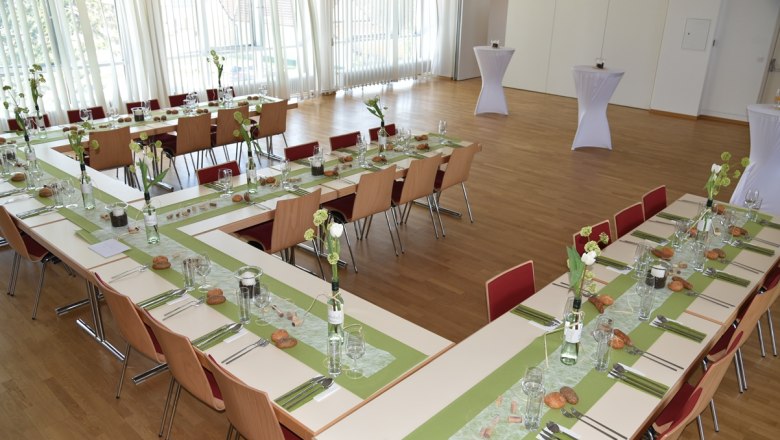 Festsaal, © Restaurant Hacker's Ein festlich gedeckter Saal mit U-förmig angeordneten Tischen, grünen Tischläufern und Blumendekoration.