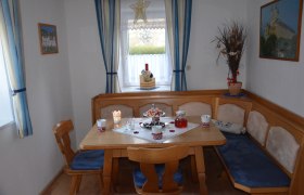 esszimmer_1, © Karl Temper Gemütliches Esszimmer mit Holztisch, Eckbank und blauen Polstern. Fenster mit blauen Vorhängen und weihnachtlicher Dekoration.